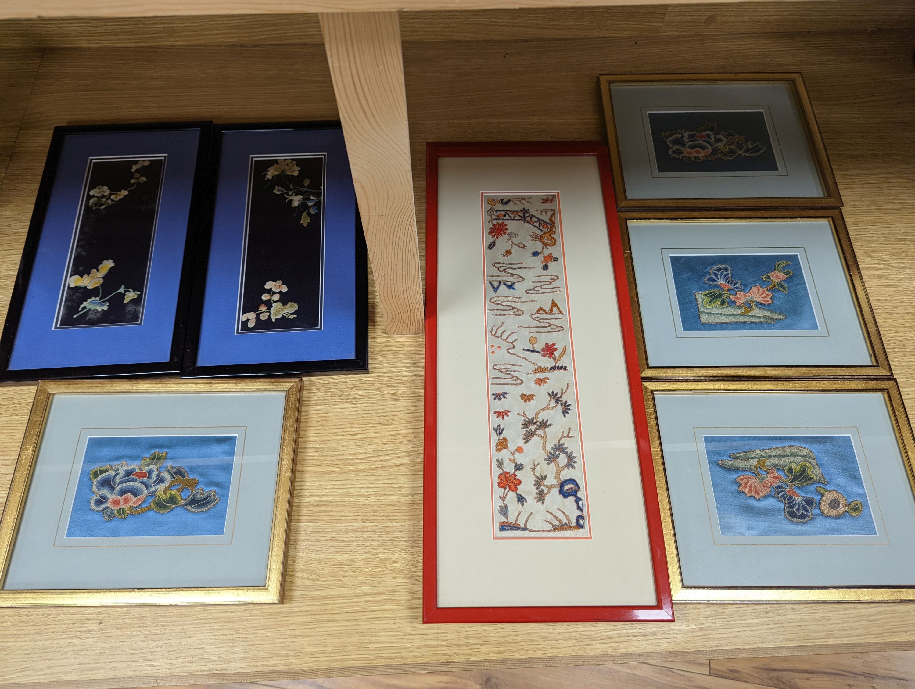 A set of four Chinese silk embroidered motifs, a pair of floral silk motifs and a later pair f sleeve bands, all framed